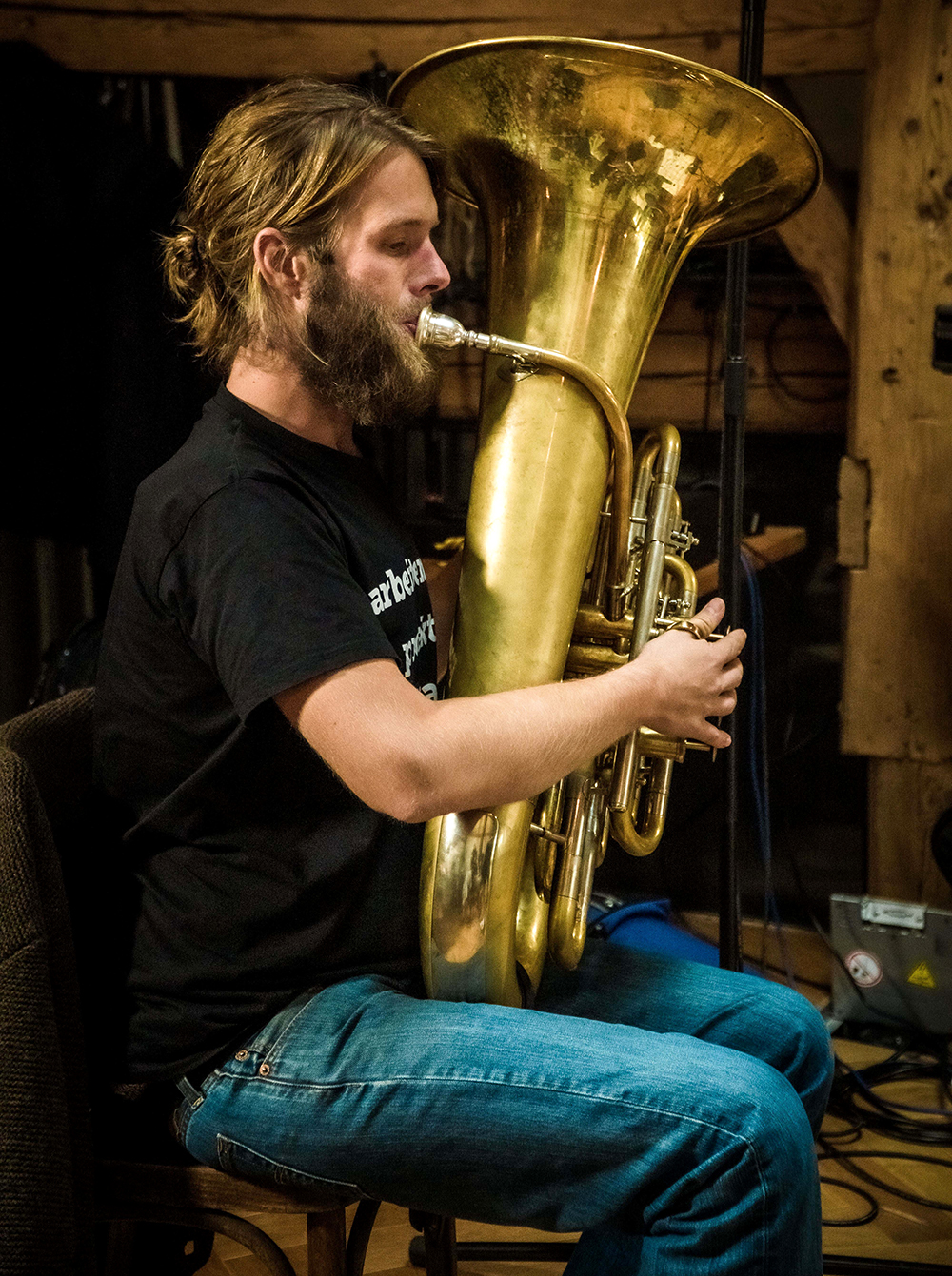 Stefan Huber beim Tuba spielen. Er sitzt dabei auf einem Stuhl und ist von der Seite fototgrafiert. Foto (c) Sebastian Huber jun.